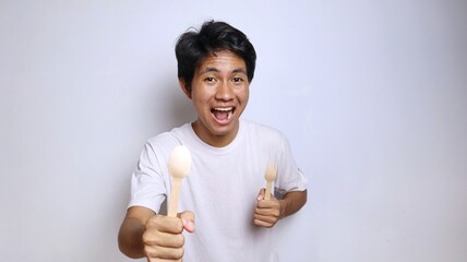 excited young asian man in white shirt gestures holding spoon and fork made of bamboo