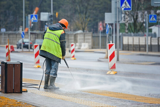 Construction worker cleaning city sidewalk with pressure washer after laying tactile paving slabs at bus stop, remove debris from sidewalk, street maintenance and public sanitation in the city