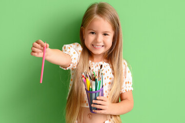 Cute little girl with pen cup on green background