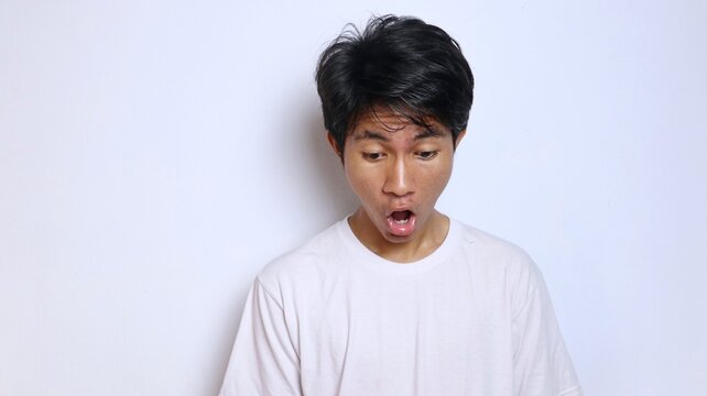 Young Asian man in white shirt with funny shocked gesture looking down - Powered by Adobe