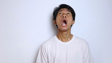 Young Asian man in white shirt with funny shocked gesture looking up