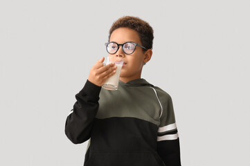 Little African-American boy with glass cup of milk on white background