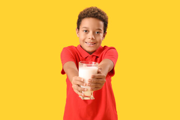 Little African-American boy with glass of milk on yellow background