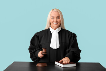 Mature female judge with gavel and book at table on blue background