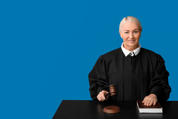 Mature female judge with gavel and book at table on blue background