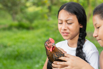 Latina peasant brunette girl, holding a chicken while looking at it with displeasure