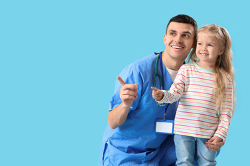 Male pediatrician and little girl pointing at something on blue background