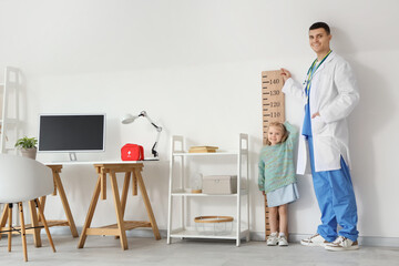 Male pediatrician measuring height of little girl in clinic