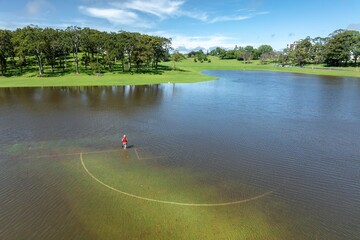 Person crossing a flooded sports field from severe summer storms in the Auckland Domain, Auckland, Auckland, New Zealand.