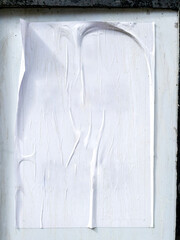 A wrinkled white poster pasted carelessly on a stone wall, showing signs of wear and weathering.