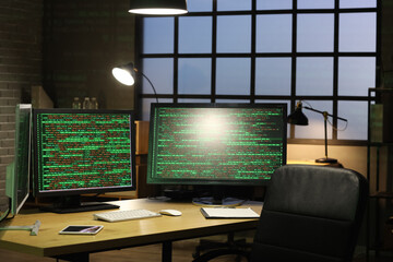Computer monitors with programming code on desk in office at night
