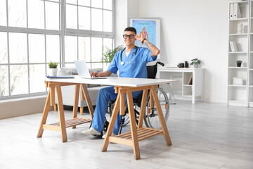 Young male doctor in wheelchair working at his workspace in clinic