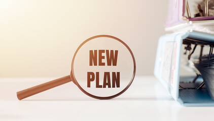 A magnifying glass focusing on the term New Plan signifies the concept of scrutinizing or...