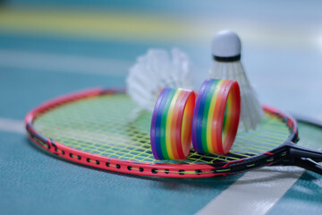 Rainbow wristbands, used cream white badminton shuttlecock and racket placed on floor in indoor...