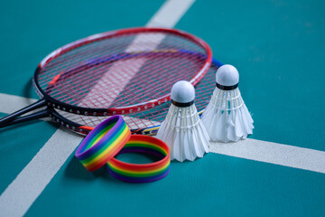 Rainbow wristbands, used cream white badminton shuttlecock and racket placed on floor in indoor badminton court, copy space, soft and selective focus on shuttlecocks.
