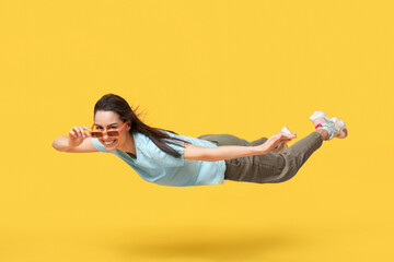 Joyful young woman in sunglasses flying on yellow background
