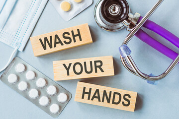 In the foreground, wooden blocks spell Wash Your Hands with a stethoscope and pills nearby,...