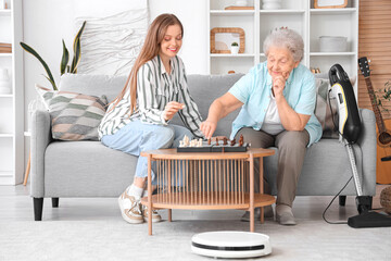 Senior woman and her granddaughter playing chess with robot vacuum cleaner at home