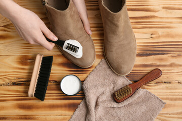 Hands cleaning shoes with brush on wooden background