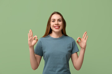 Young deaf mute woman using sign language on green background