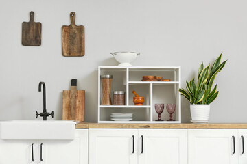 White kitchen counters with sink, utensils and houseplant near white wall