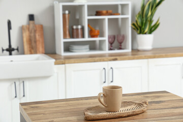 Wooden counter with cutting board and cup in interior of light kitchen