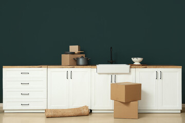 Interior of modern kitchen with white counters, rolled rug and cardboard boxes. Moving house concept