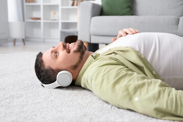 Young man in headphones lying on soft carpet at home, closeup