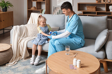 Male pediatrician measuring temperature of little girl with infrared thermometer at home