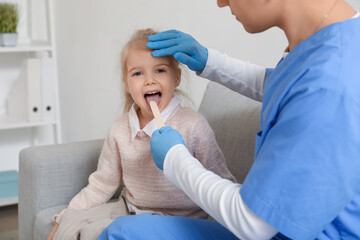 Male pediatrician examining little girl with tongue depressor in clinic