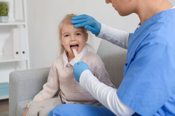 Male pediatrician examining little girl with tongue depressor in clinic © Pixel-Shot