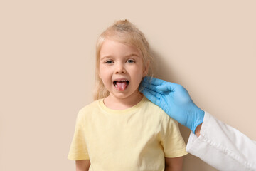 Pediatrician examining little girl near beige wall