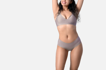 Young African-American woman in underwear on light background