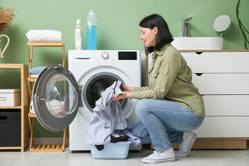Young woman putting dirty clothes into washing machine in laundry room