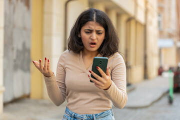 Indian woman using mobile smartphone loses becoming surprised sudden lottery casino game results receive bad message mail news fortune loss fail outdoors. Girl walking on urban city street