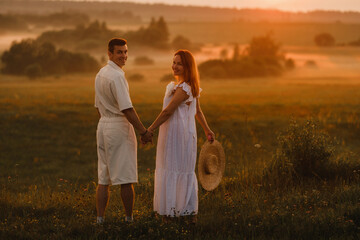 A couple in love in white clothes in a field at a red sunset