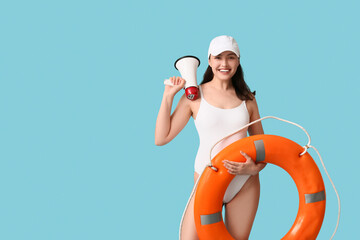Young female lifeguard with ring buoy and megaphone on blue background
