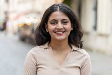 Portrait of happy Indian young woman smiling friendly glad expression looking at camera dreaming resting relaxation feel satisfied good news outdoor. Hispanic girl walking on urban city street