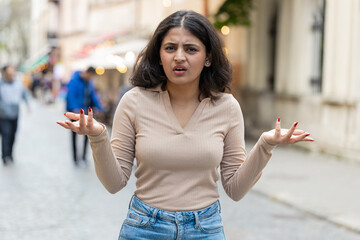 What. Why. Surprised frustrated Indian woman raising hands asking reason of failure demonstrating disbelief irritation by troubles outdoors. Confused girl walking on urban city street. Town lifestyles