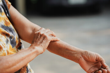 An elderly woman is holding her arm in pain.