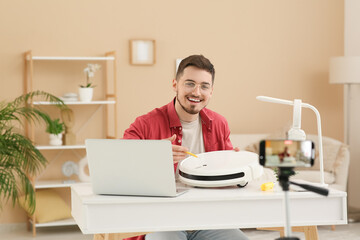 Young male blogger recording robot vacuum cleaner fixing tutorial at home