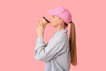Beautiful young woman in stylish cap with paper cup of coffee on pink background