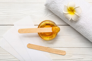 Glass bowl with sugaring paste, wax strips, sticks and beautiful flower on white wooden background