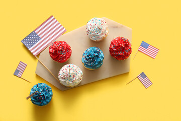 Tasty patriotic cupcakes with USA flags on yellow background. American Independence Day