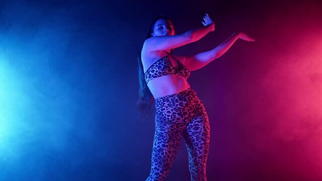 Hot woman performs sexy moves in leopard printed costume in neon light. Seductive dance in multicolor studio. Lady dancer in smoke.