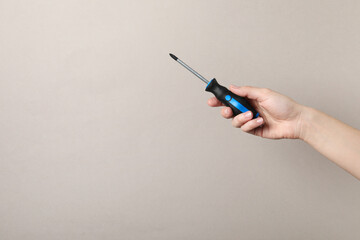 Woman holding screwdriver on grey background, closeup. Space for text