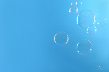 Beautiful transparent soap bubbles on light blue background, space for text