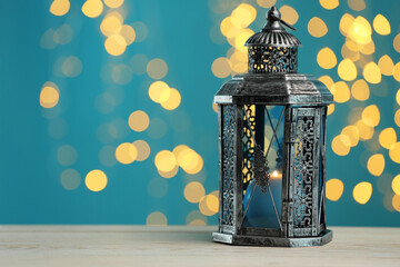 Traditional Arabic lantern on wooden table against light blue background with blurred lights. Space for text