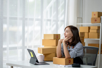 A woman is sitting at a desk with a laptop and a stack of boxes in front of her