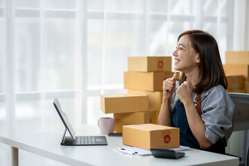 A woman is sitting at a desk with a laptop and a stack of boxes in front of her